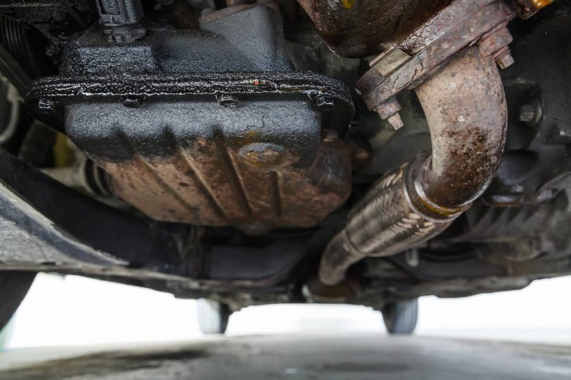 Close-up view of a car's rusted undercarriage, highlighting the exhaust pipe and oil pan. The image conveys wear and the need for maintenance.