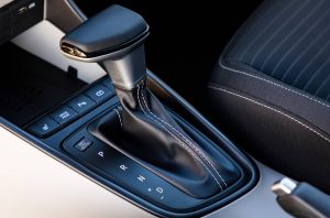 Close-up of a car's automatic gear shift in a modern interior. The leather shift boot has white stitching. Adjacent buttons control seat heating.
